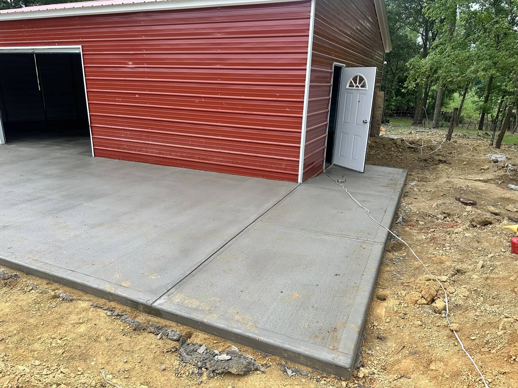 Driveway preparation: concrete apron beside a red outbuilding and graded open ground