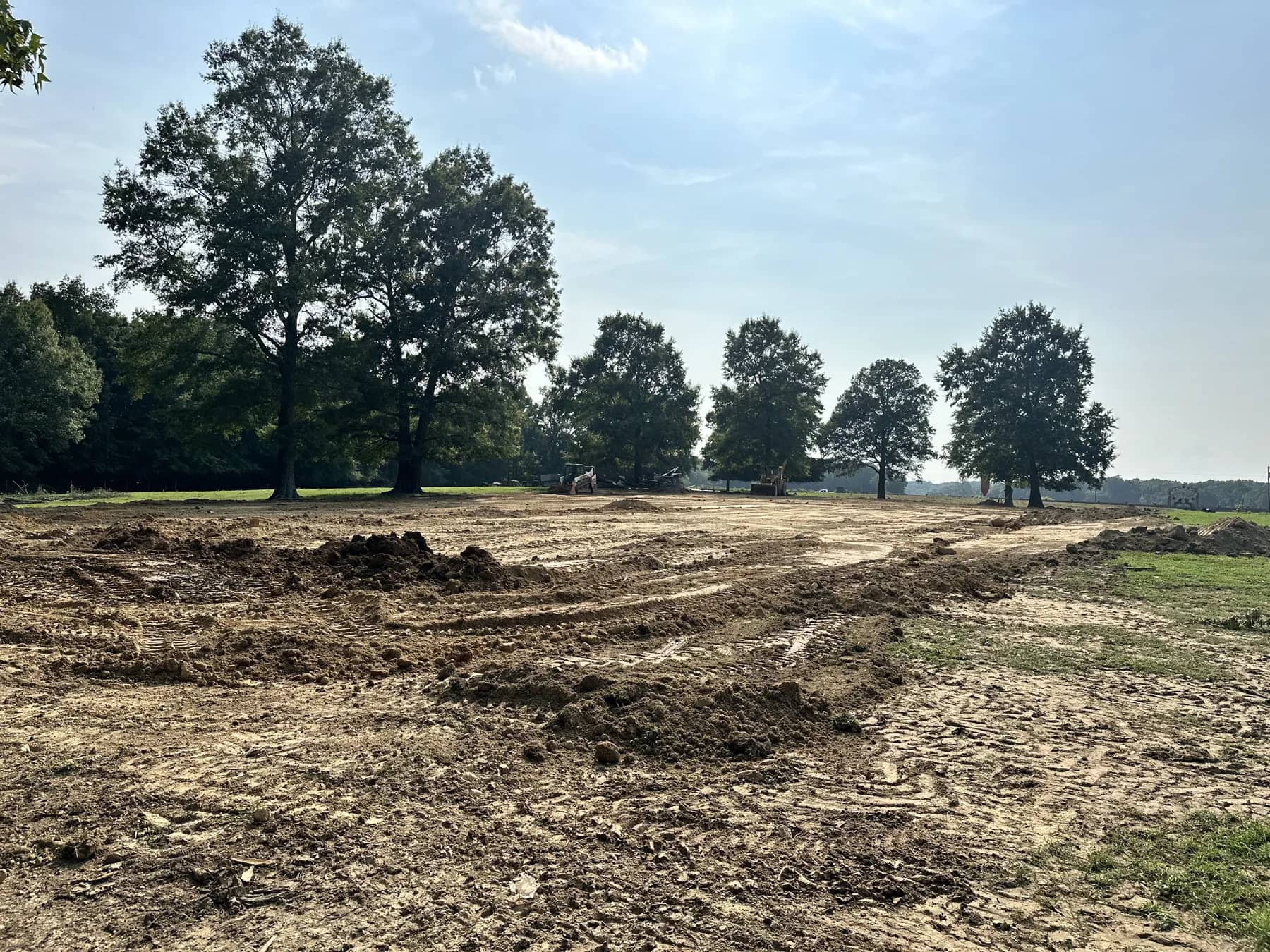 Land clearing result: open, graded acreage with exposed soil and mature trees left standing